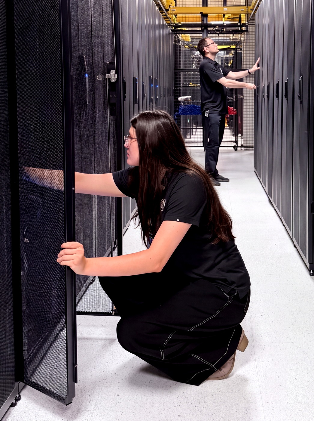 An Opus Interactive engineer opening a rack door in a cold aisle while a colleague works further down the row