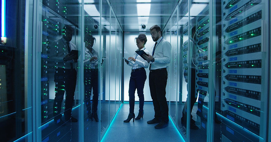 Photo of a man and woman inside a datacenter cage surrounded by cabinets and IT infrastructure